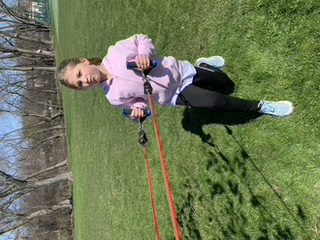 A girl pulling ropes wearing pink in a field with trees in the back
